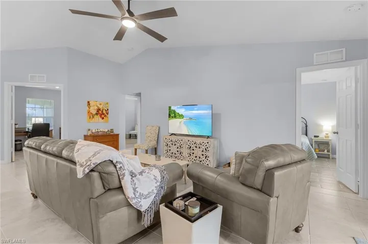 Living area with vaulted ceiling, light tile patterned floors, visible vents, and a ceiling fan