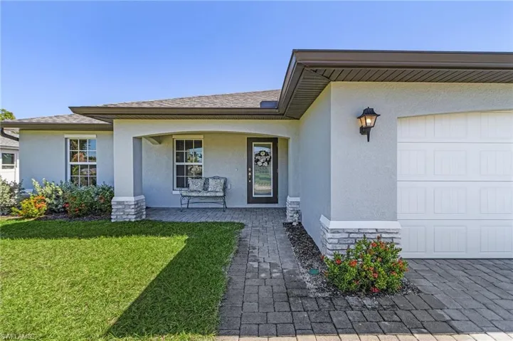 Entrance to property featuring roof with shingles, stucco siding, a porch, a lawn, and a garage