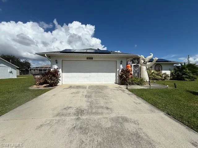 Ranch-style house featuring a front yard, a garage, driveway, and roof mounted solar panels