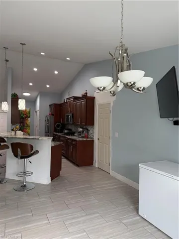 Kitchen with a breakfast bar area, light stone countertops, fridge, lofted ceiling, and hanging lights