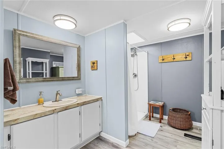 Full bathroom with vanity, light wood-style flooring, a shower stall, and crown molding