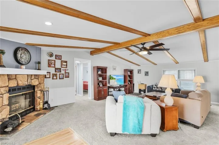 Living area featuring a fireplace, light colored carpet, and ceiling fan.