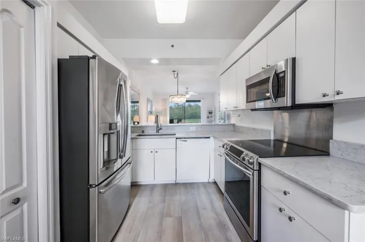 Kitchen featuring stainless steel appliances, light wood-style flooring, white cabinetry, and pendant lighting