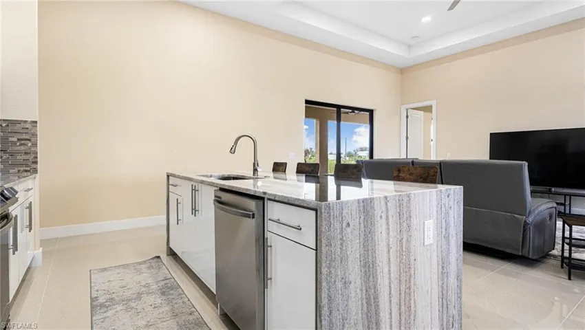 Kitchen with light stone countertops, a kitchen island with sink, a sink, stainless steel dishwasher, and backsplash