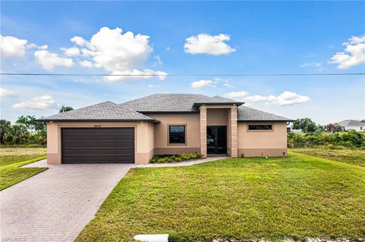View of front of home featuring a front yard, decorative driveway, a garage, and stucco siding