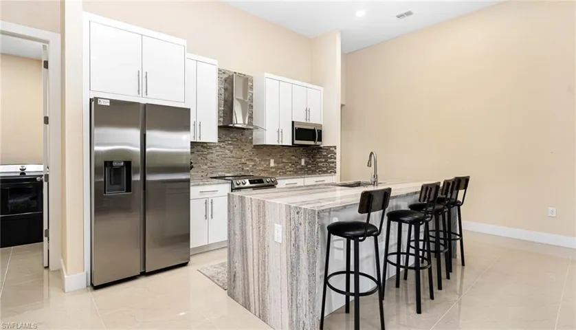 Kitchen featuring a sink, decorative backsplash, stainless steel appliances, white cabinets, and wall chimney exhaust hood