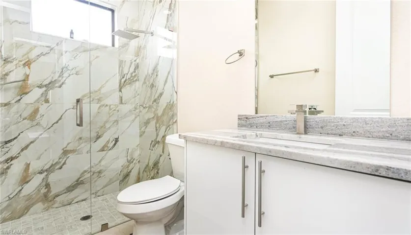 Full bath with a marble finish shower, toilet, and vanity