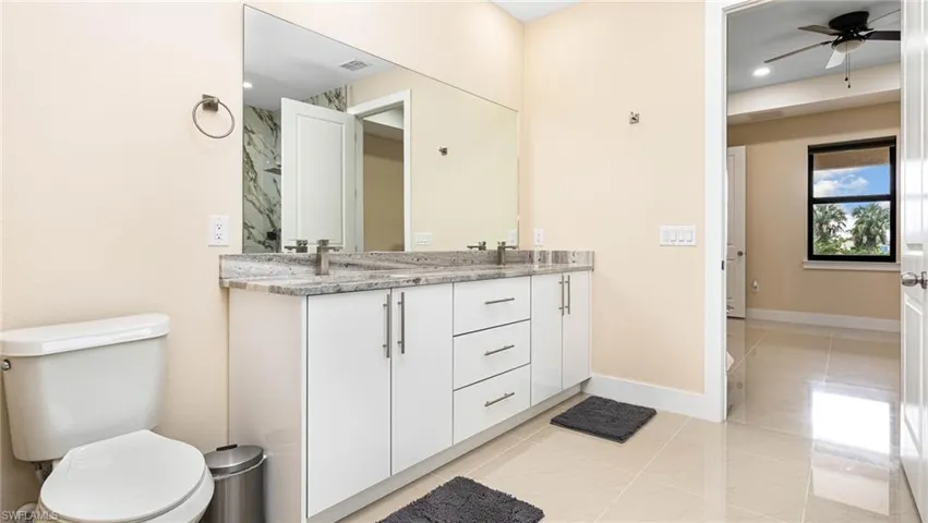 Full bathroom with visible vents, baseboards, double vanity, ceiling fan, and toilet