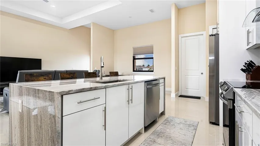 Kitchen with a sink, light stone counters, an island with sink, and stainless steel appliances