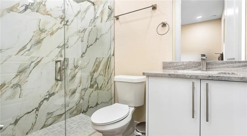 Full bath with a marble finish shower, toilet, and vanity