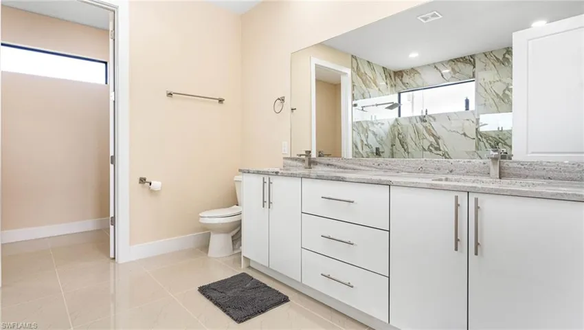 Bathroom with a marble finish shower, baseboards, toilet, double vanity, and a sink