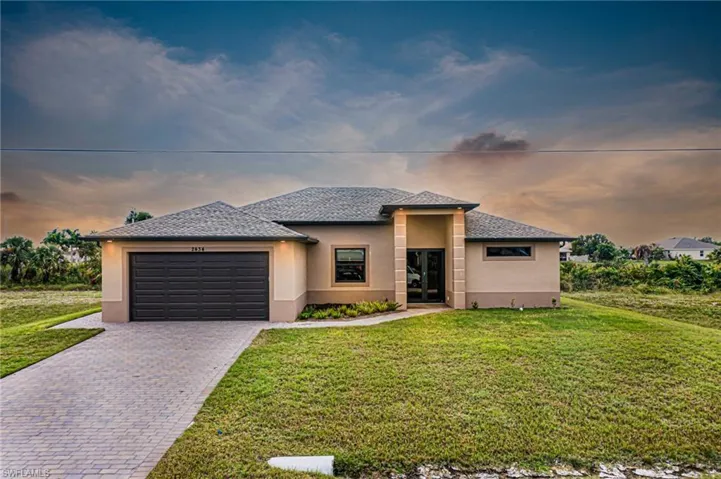Prairie-style home with decorative driveway, a yard, an attached garage, and stucco siding