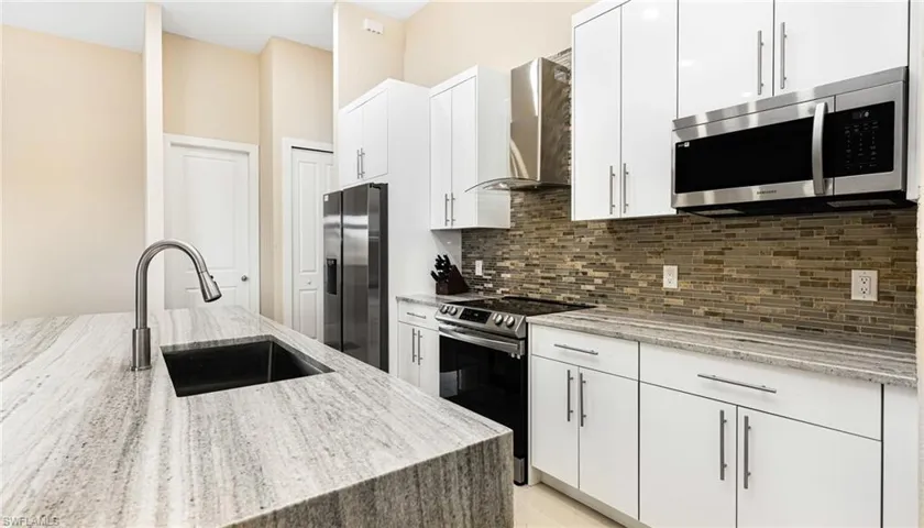 Kitchen with a sink, tasteful backsplash, stainless steel appliances, white cabinets, and wall chimney range hood