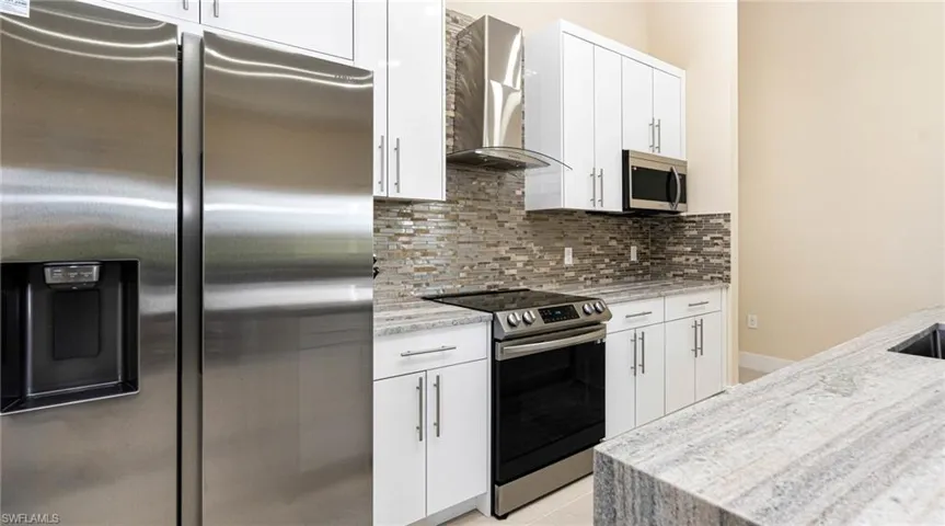Kitchen with stainless steel appliances, backsplash, white cabinets, and wall chimney range hood