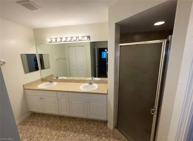 Bathroom featuring a shower with shower door, tile flooring, large vanity, and dual sinks