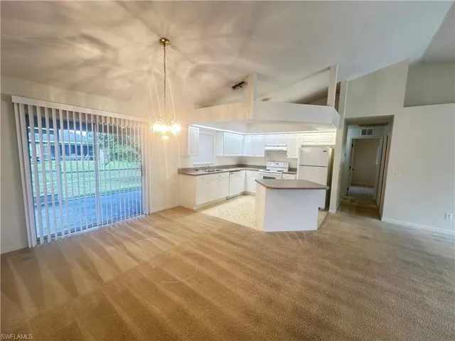 Kitchen with white appliances, vaulted ceiling, light colored carpet, hanging light fixtures, and white cabinetry