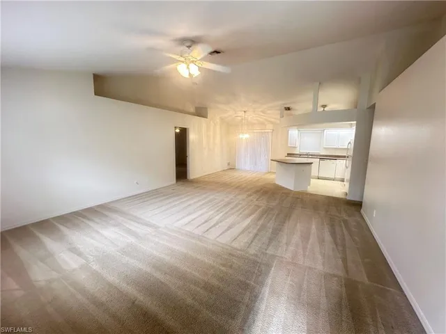 Unfurnished living room with ceiling fan, vaulted ceiling, and light colored carpet