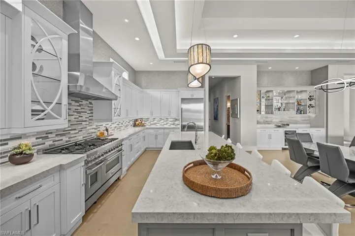 Kitchen with tasteful backsplash, wall chimney range hood, light wood-type flooring, a spacious island, and high quality appliances