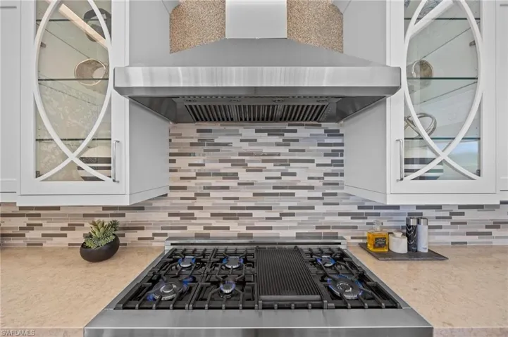Kitchen with black range oven, white cabinetry, wall chimney range hood, and tasteful backsplash