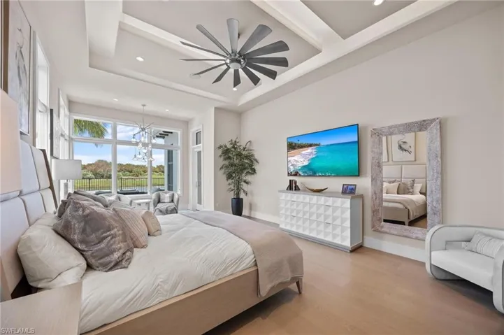 Bedroom with light hardwood / wood-style floors, a tray ceiling, and ceiling fan with notable chandelier