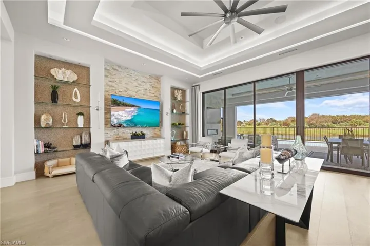 Living room featuring ceiling fan, a tray ceiling, light hardwood / wood-style flooring, and built in shelves