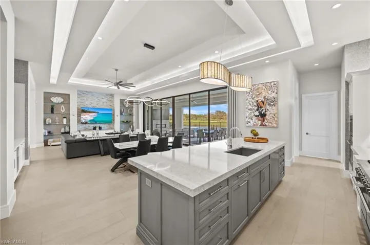 Kitchen with a kitchen island with sink, a tray ceiling, light wood-type flooring, and gray cabinetry