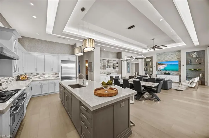 Kitchen with high quality appliances, a large island, decorative light fixtures, a raised ceiling, and white cabinetry