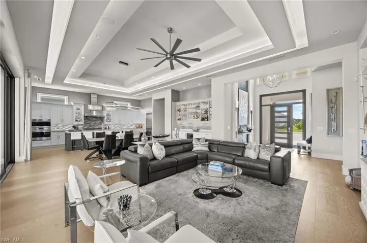 Living room with ceiling fan with notable chandelier, a tray ceiling, and light wood-type flooring