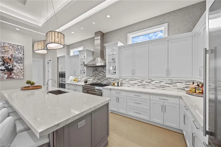 Kitchen with wall chimney exhaust hood, high quality appliances, white cabinetry, and plenty of natural light