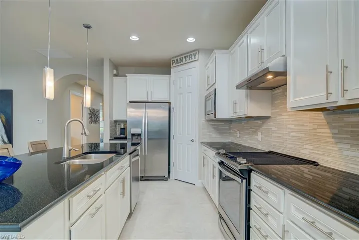 Kitchen featuring stainless steel appliances, white cabinetry, decorative backsplash, pendant lighting, and under cabinet range hood