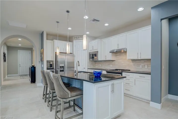 Kitchen with white cabinets, a kitchen breakfast bar, a kitchen island with sink, arched walkways, and recessed lighting