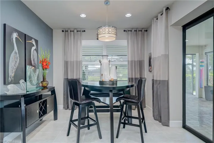 Tiled dining space with recessed lighting, decorative window treatments and baseboards. Zero edge doors open to lanai area and large windows overlook the pool