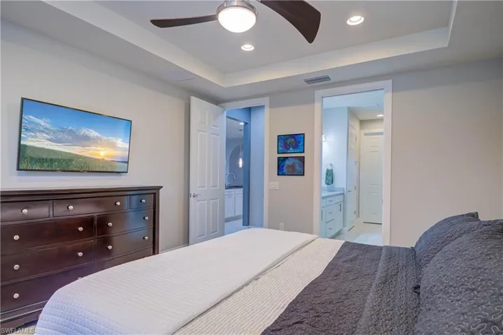 Bedroom with a tray ceiling, a ceiling fan, recessed lighting, and ensuite bath