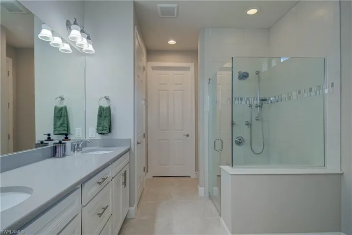 Full bath featuring double vanity, a stall shower, light tile patterned floors, recessed lighting, large walk-in closet, and storage