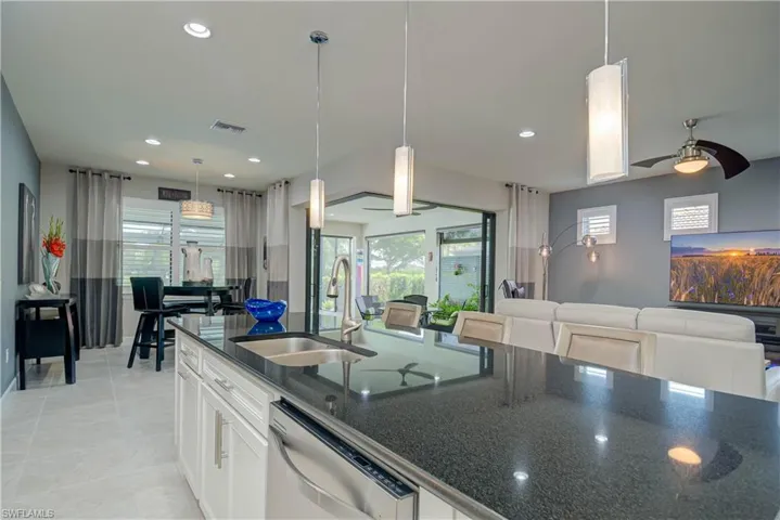 Kitchen with white cabinets, dark stone countertops, stainless steel dishwasher, hanging light fixtures, and open floor plan Open living room & dining for entertaining-  with recessed lighting, a ceiling fan, and light tile patterned floors. Zero edge doors make indoor/outdoor flow easy to the lanai area and pool