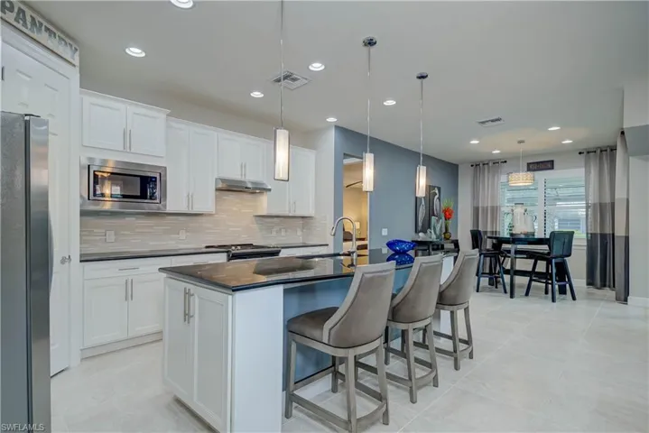 Kitchen featuring tasteful backsplash, stainless steel appliances, a kitchen island with sink, white cabinets, and decorative light fixtures. Split bedrooms with primary just behind the kitchen area.