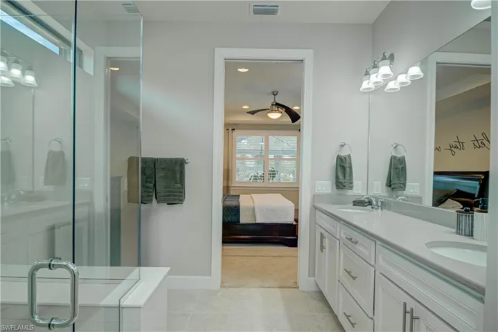 Ensuite bathroom with double vanity, a shower stall, light tile patterned floors, and a ceiling fan