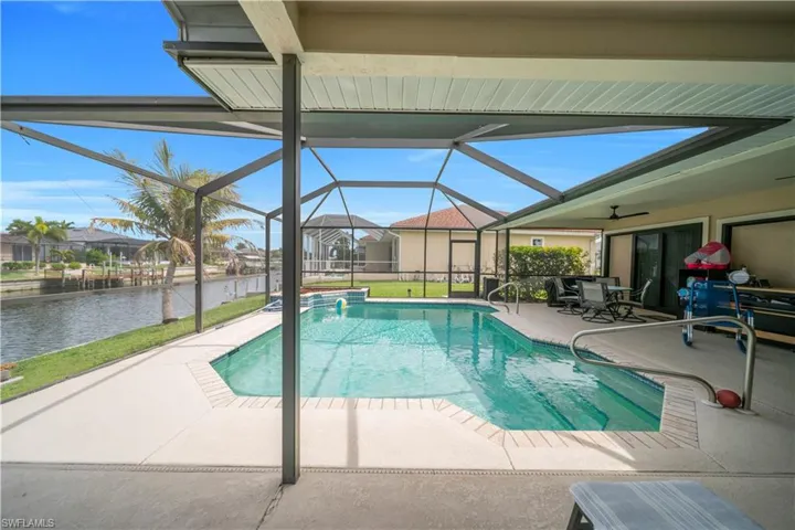 Outdoor pool featuring a patio, a sunroom, glass enclosure, outdoor dining area, and a water view