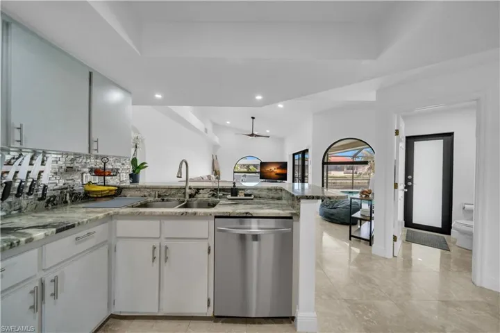 Kitchen featuring dishwasher, a peninsula, ceiling fan, backsplash, and light stone counters