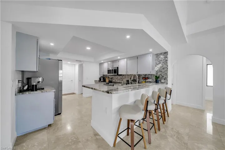 Kitchen with arched walkways, a peninsula, a breakfast bar, a tray ceiling, and light stone counters