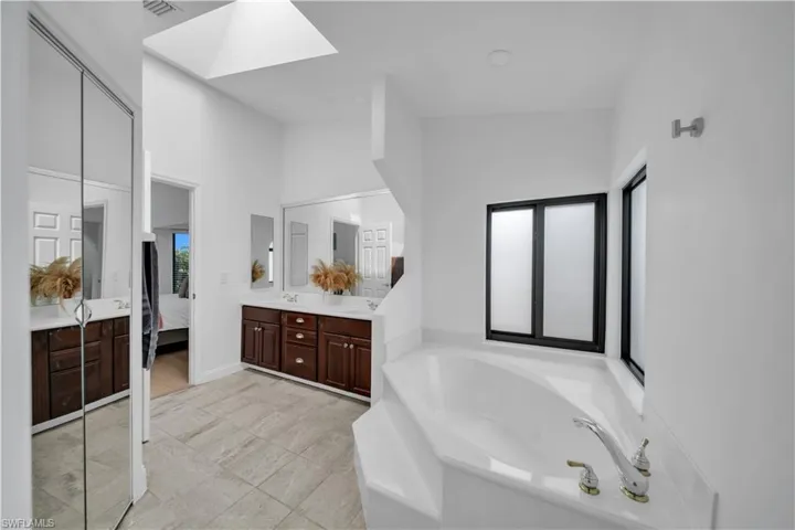 Bathroom with double vanity, a skylight, connected bathroom, a bath, and a high ceiling