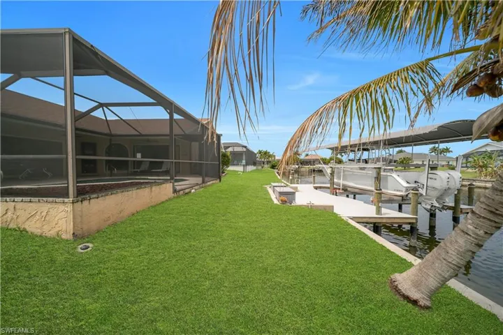 Dock featuring a lanai, a lawn, a water view, boat lift, and a sunroom