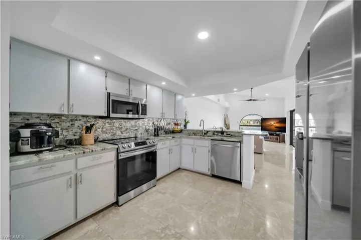 Kitchen with stainless steel appliances, light stone counters, a peninsula, open floor plan, and ceiling fan
