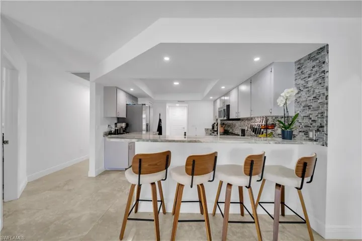 Kitchen featuring a breakfast bar, a raised ceiling, a peninsula, backsplash, and freestanding refrigerator
