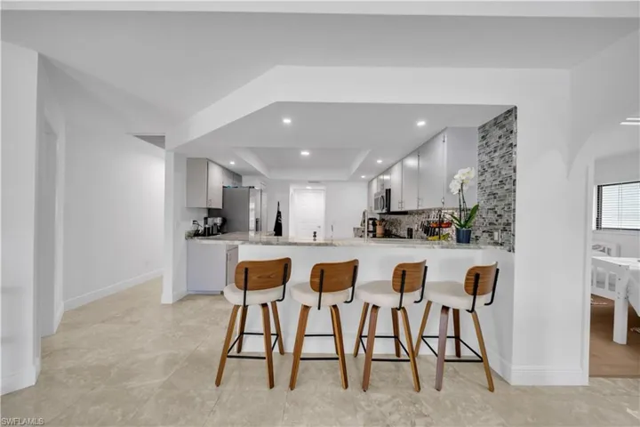 Kitchen featuring a kitchen breakfast bar, a raised ceiling, light stone counters, a peninsula, and arched walkways