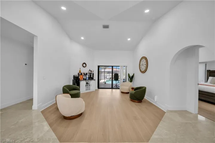 Living area with light wood-style floors, recessed lighting, arched walkways, and vaulted ceiling