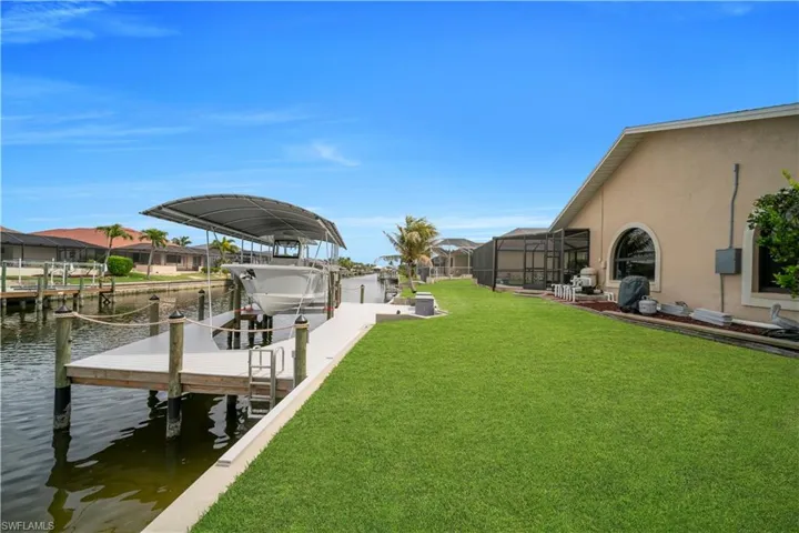 Dock area featuring glass enclosure, boat lift, a water view, a lawn, and a sunroom