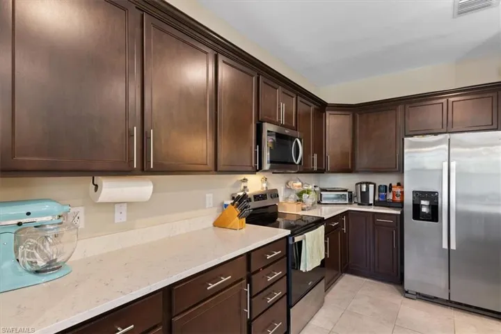Kitchen featuring dark brown cabinetry, stainless steel appliances, light stone counters, and light tile floors