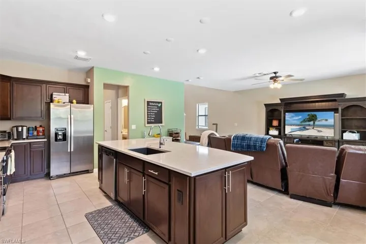 Kitchen with ceiling fan, an island with sink, stainless steel appliances, light tile floors, and sink