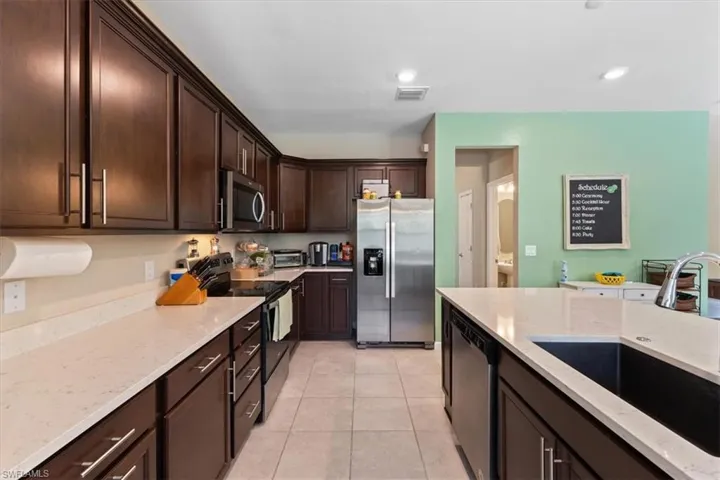 Kitchen with light stone countertops, dark brown cabinets, appliances with stainless steel finishes, sink, and light tile floors
